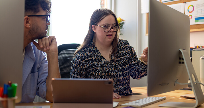 A teenage girl with Downs Syndrome working on a desktop computer with a male practitioner