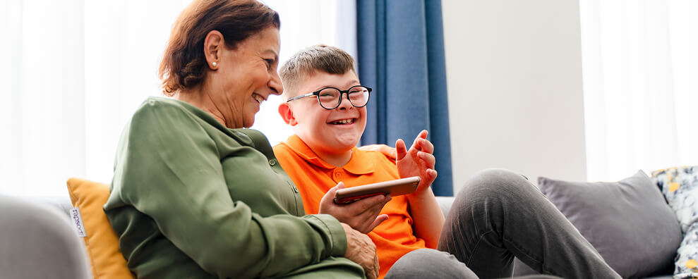 A mother and son smiling. The boy is holding a phone in his hand