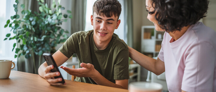 A teenage boy talking with an adult, smiling at his mobile phone